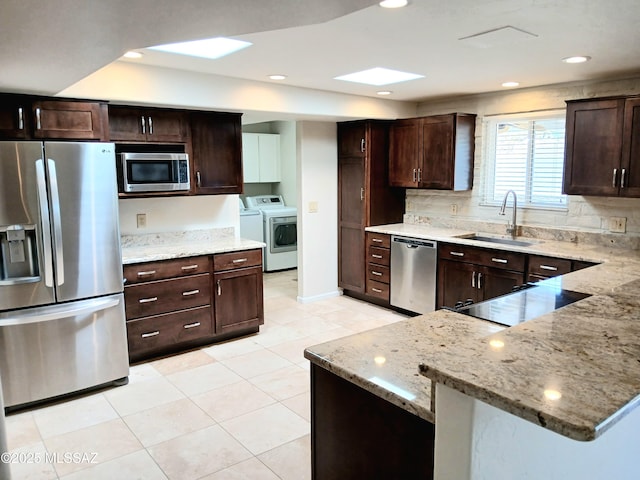 kitchen with stainless steel appliances, washing machine and dryer, a sink, and light stone counters