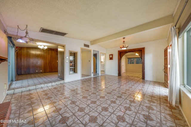 unfurnished room featuring arched walkways, visible vents, wood walls, and a textured ceiling