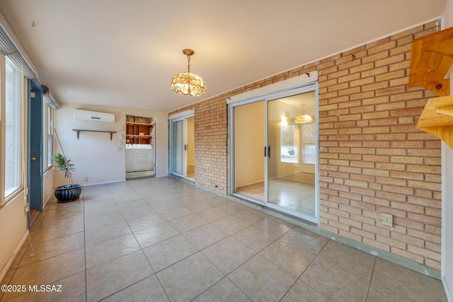 interior space featuring washer / dryer, baseboards, brick wall, tile patterned flooring, and an AC wall unit