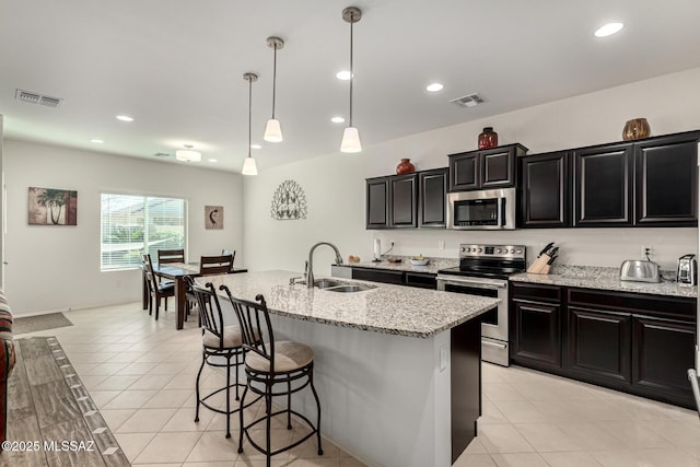 kitchen with light tile patterned flooring, sink, appliances with stainless steel finishes, an island with sink, and pendant lighting