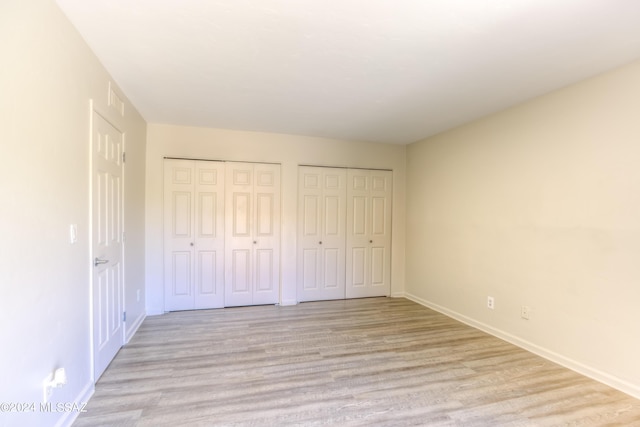 unfurnished bedroom featuring two closets and light wood-type flooring