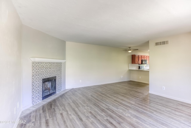 unfurnished living room featuring a tile fireplace, ceiling fan, and light hardwood / wood-style flooring