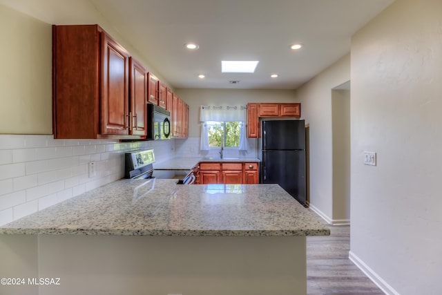 kitchen featuring light wood-type flooring, black appliances, light stone counters, and kitchen peninsula