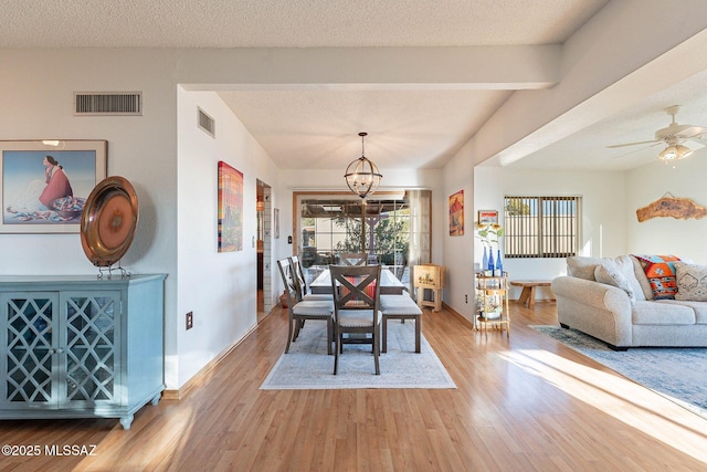 dining room with ceiling fan with notable chandelier, light hardwood / wood-style floors, and a textured ceiling