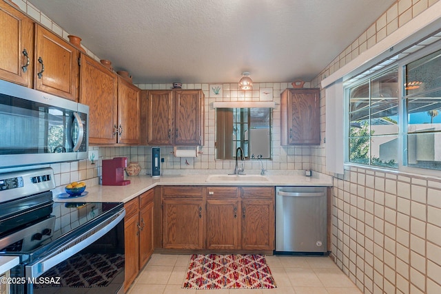 kitchen featuring sink, light tile patterned floors, appliances with stainless steel finishes, and a textured ceiling