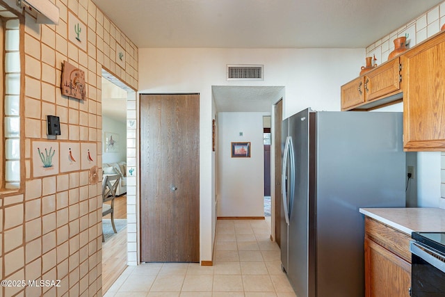 kitchen featuring light tile patterned flooring, stainless steel refrigerator, tile walls, and electric stove