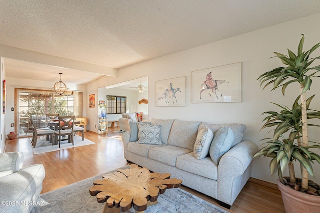 living room with light wood-type flooring, ceiling fan with notable chandelier, beam ceiling, and a textured ceiling