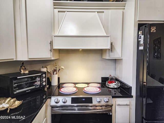 kitchen featuring stainless steel range with electric stovetop, white cabinets, black fridge, and premium range hood