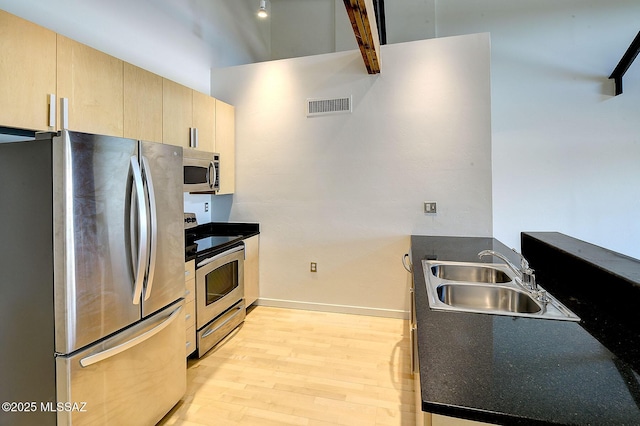 kitchen with appliances with stainless steel finishes, light hardwood / wood-style floors, light brown cabinetry, and sink