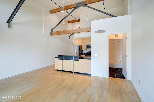 unfurnished living room with a high ceiling, light hardwood / wood-style floors, and beamed ceiling