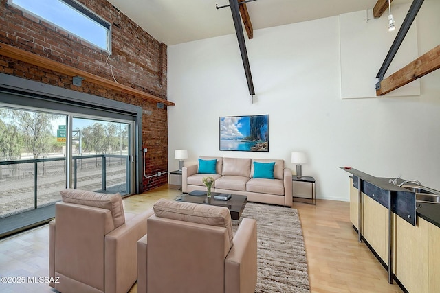 living room with beamed ceiling, a towering ceiling, light hardwood / wood-style floors, and brick wall