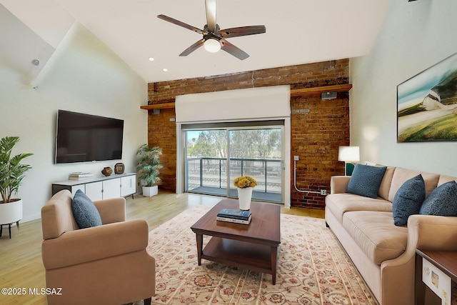 living room with ceiling fan, brick wall, light wood-type flooring, and high vaulted ceiling