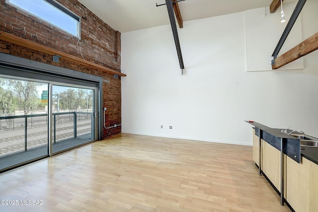 unfurnished living room with a high ceiling, beamed ceiling, brick wall, and light wood-type flooring