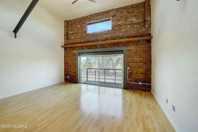 unfurnished living room with a high ceiling, light wood-type flooring, and brick wall