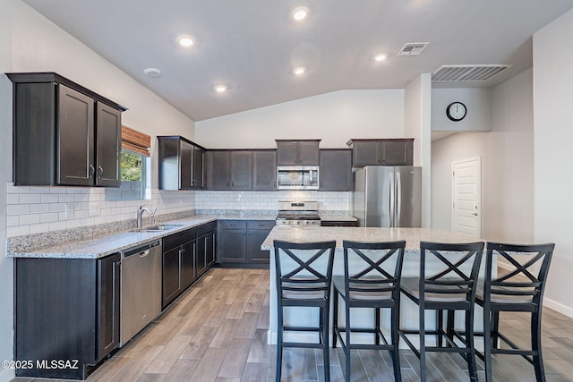 kitchen with vaulted ceiling, a center island, light wood-type flooring, appliances with stainless steel finishes, and sink