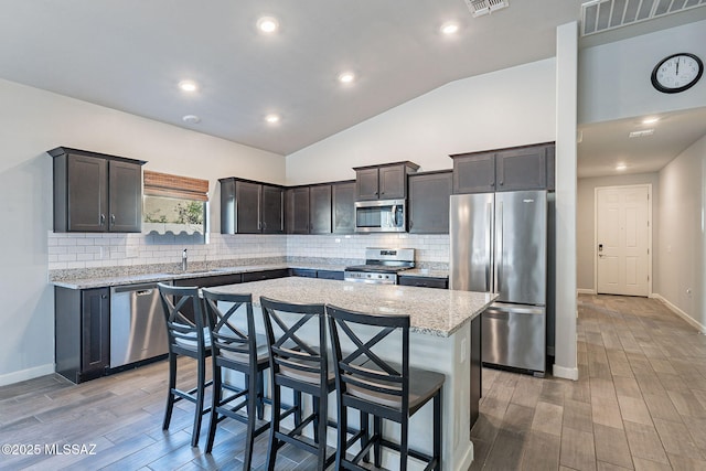 kitchen with appliances with stainless steel finishes, light hardwood / wood-style floors, a kitchen island, and dark brown cabinetry