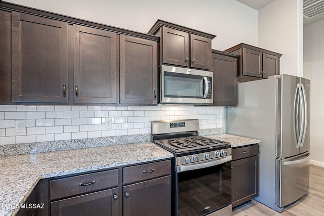 kitchen with stainless steel appliances, light hardwood / wood-style floors, light stone countertops, backsplash, and dark brown cabinetry