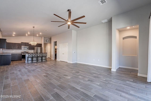 unfurnished living room with sink, vaulted ceiling, and ceiling fan with notable chandelier