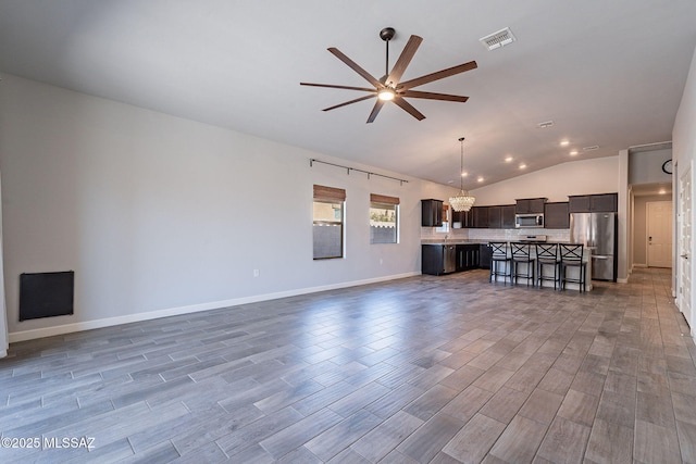 unfurnished living room with ceiling fan with notable chandelier and vaulted ceiling