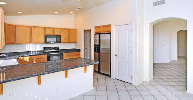 kitchen featuring a breakfast bar, black appliances, light tile patterned floors, high vaulted ceiling, and dark stone countertops