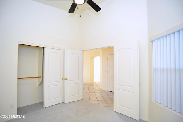 unfurnished bedroom featuring light carpet, a towering ceiling, a closet, and ceiling fan