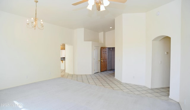 tiled empty room with ceiling fan with notable chandelier and a high ceiling