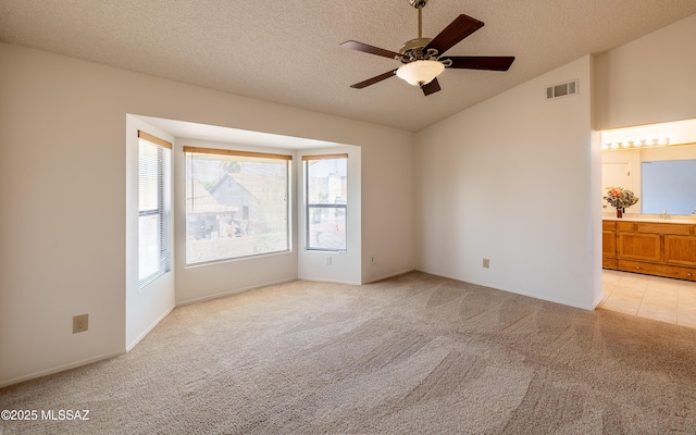 spare room featuring visible vents, a sink, ceiling fan, vaulted ceiling, and light carpet