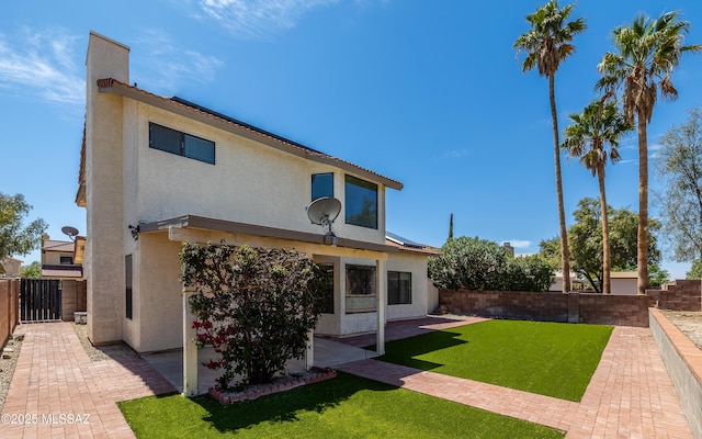 rear view of property featuring a patio area, stucco siding, a fenced backyard, and a lawn