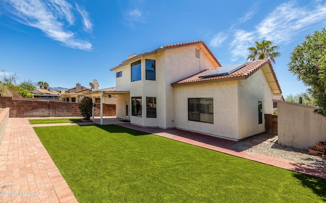 rear view of property featuring a patio, a fenced backyard, solar panels, a yard, and a tiled roof