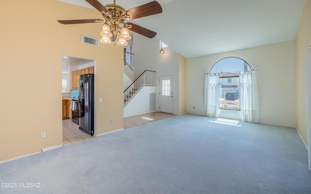 unfurnished living room with high vaulted ceiling, ceiling fan, light colored carpet, visible vents, and stairs