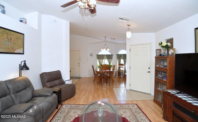 living room featuring ceiling fan with notable chandelier, light wood-type flooring, and vaulted ceiling