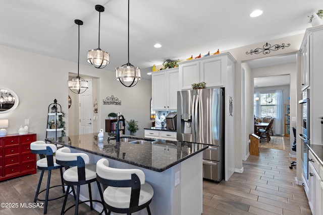 kitchen with decorative light fixtures, an island with sink, stainless steel refrigerator with ice dispenser, white cabinets, and sink