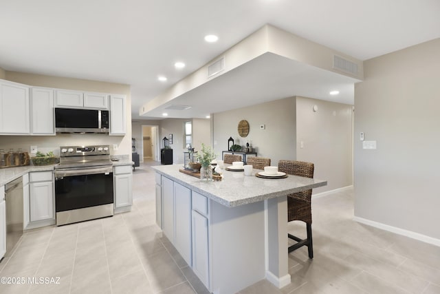 kitchen featuring stainless steel appliances, a kitchen island, white cabinetry, and a breakfast bar