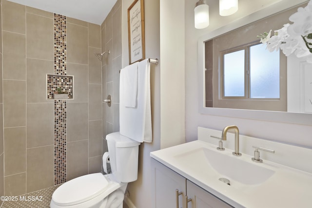 bathroom with toilet, a tile shower, and vanity