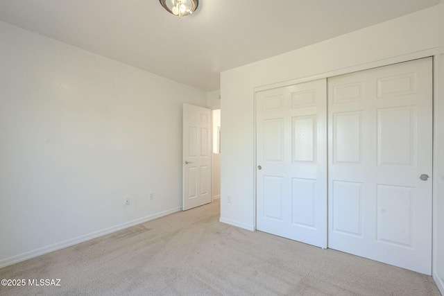 unfurnished bedroom featuring a closet, light carpet, and baseboards