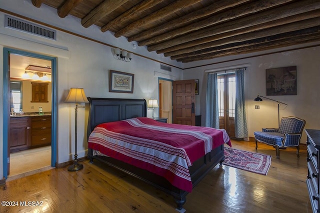 bedroom featuring beamed ceiling, ensuite bathroom, hardwood / wood-style floors, and multiple windows