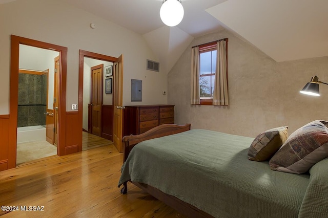 bedroom featuring electric panel, ensuite bathroom, light hardwood / wood-style flooring, and vaulted ceiling