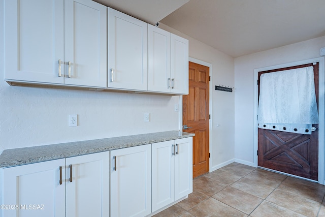 kitchen with light tile patterned floors, white cabinetry, and light stone counters