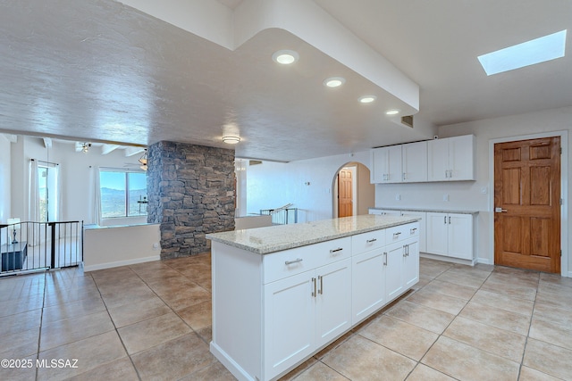 kitchen with a center island, a skylight, ceiling fan, light stone counters, and white cabinetry