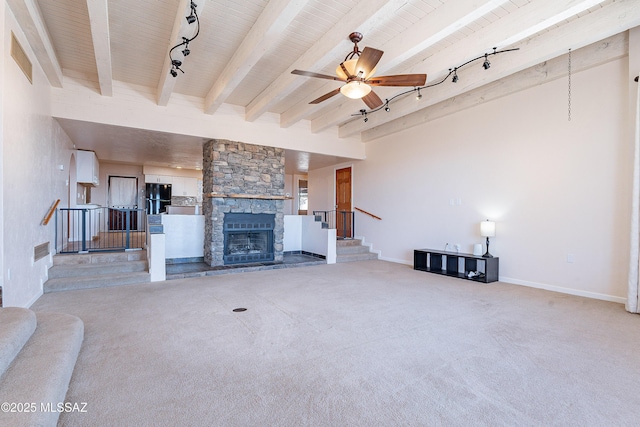 unfurnished living room featuring track lighting, wood ceiling, ceiling fan, beam ceiling, and a stone fireplace