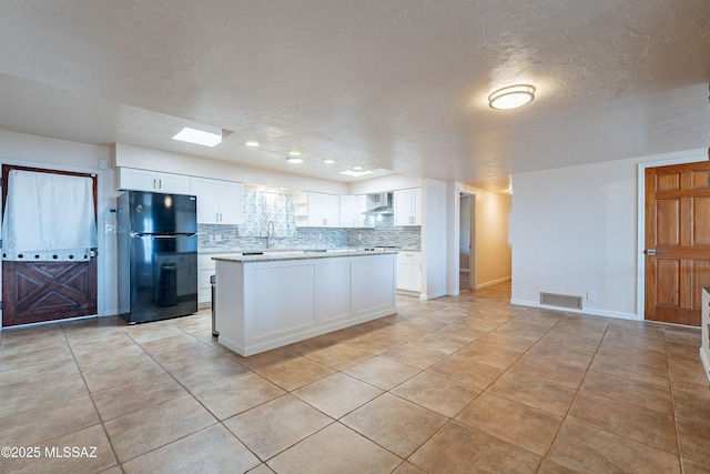 kitchen with wall chimney range hood, tasteful backsplash, a textured ceiling, black refrigerator, and white cabinets