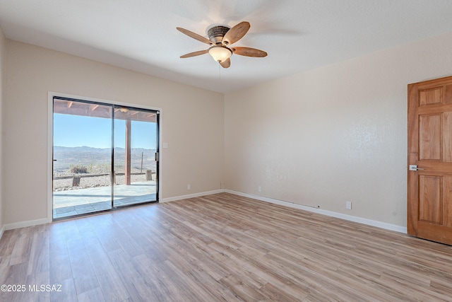 empty room featuring a mountain view, light wood-type flooring, and ceiling fan