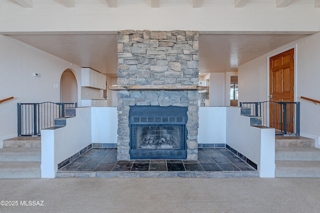 unfurnished living room featuring a fireplace, dark carpet, and beamed ceiling