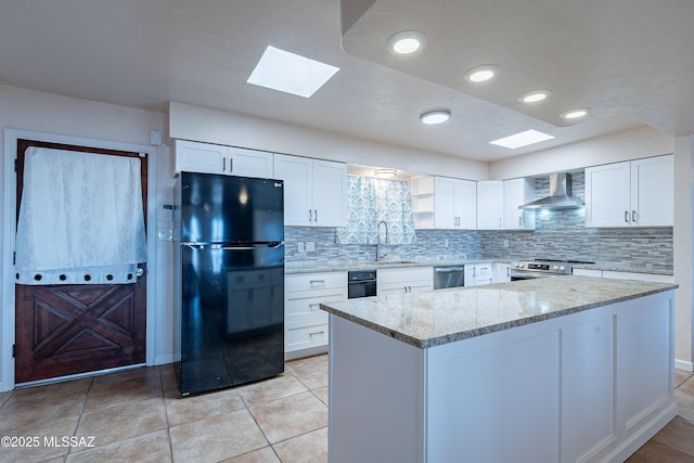 kitchen featuring a skylight, light stone countertops, stainless steel appliances, wall chimney range hood, and white cabinets