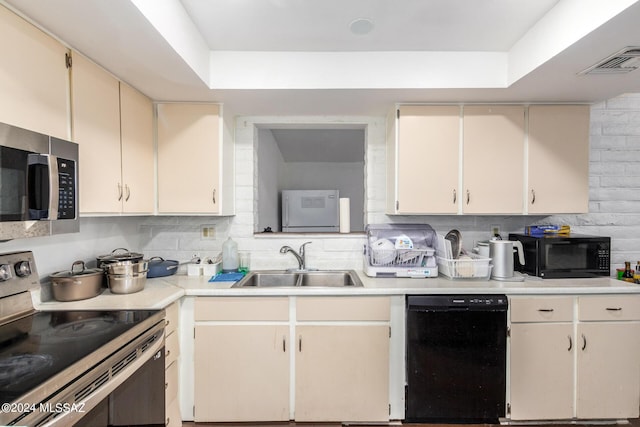 kitchen with sink, tasteful backsplash, cream cabinets, black appliances, and a raised ceiling