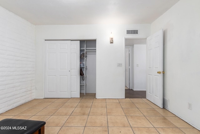 unfurnished bedroom with light tile patterned floors, a closet, and brick wall