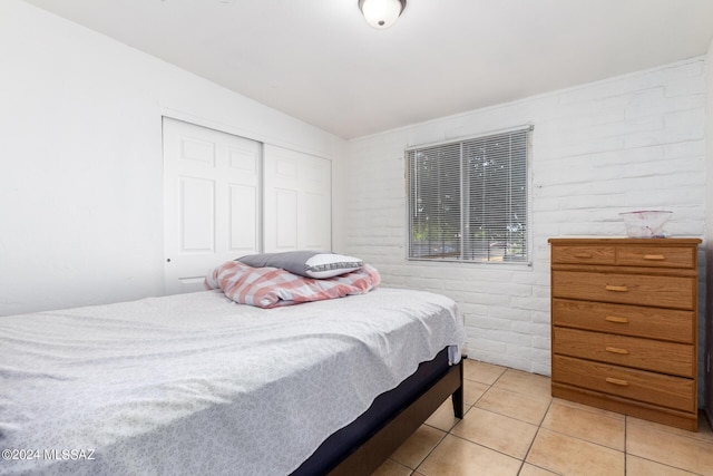 bedroom featuring light tile patterned floors, a closet, and brick wall