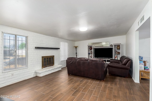 living room with brick wall, dark hardwood / wood-style floors, and a fireplace