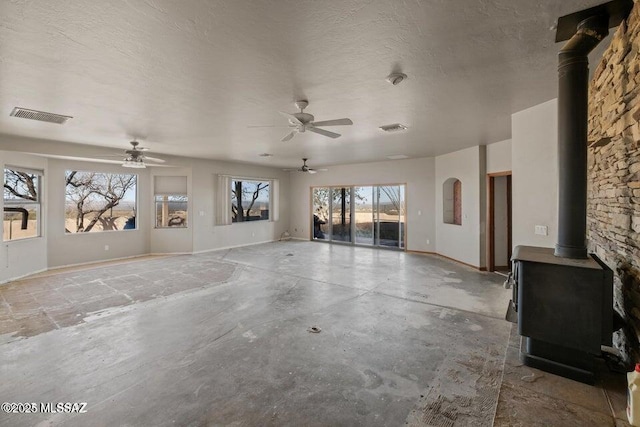 unfurnished living room with concrete floors, a wood stove, and ceiling fan