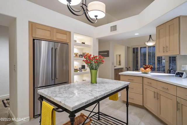 kitchen with light brown cabinetry, hanging light fixtures, stainless steel fridge, and light tile patterned flooring